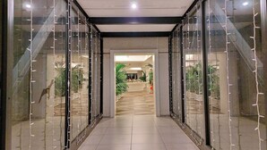 A corridor with glass walls, leading to a reception area with plants and a counter.