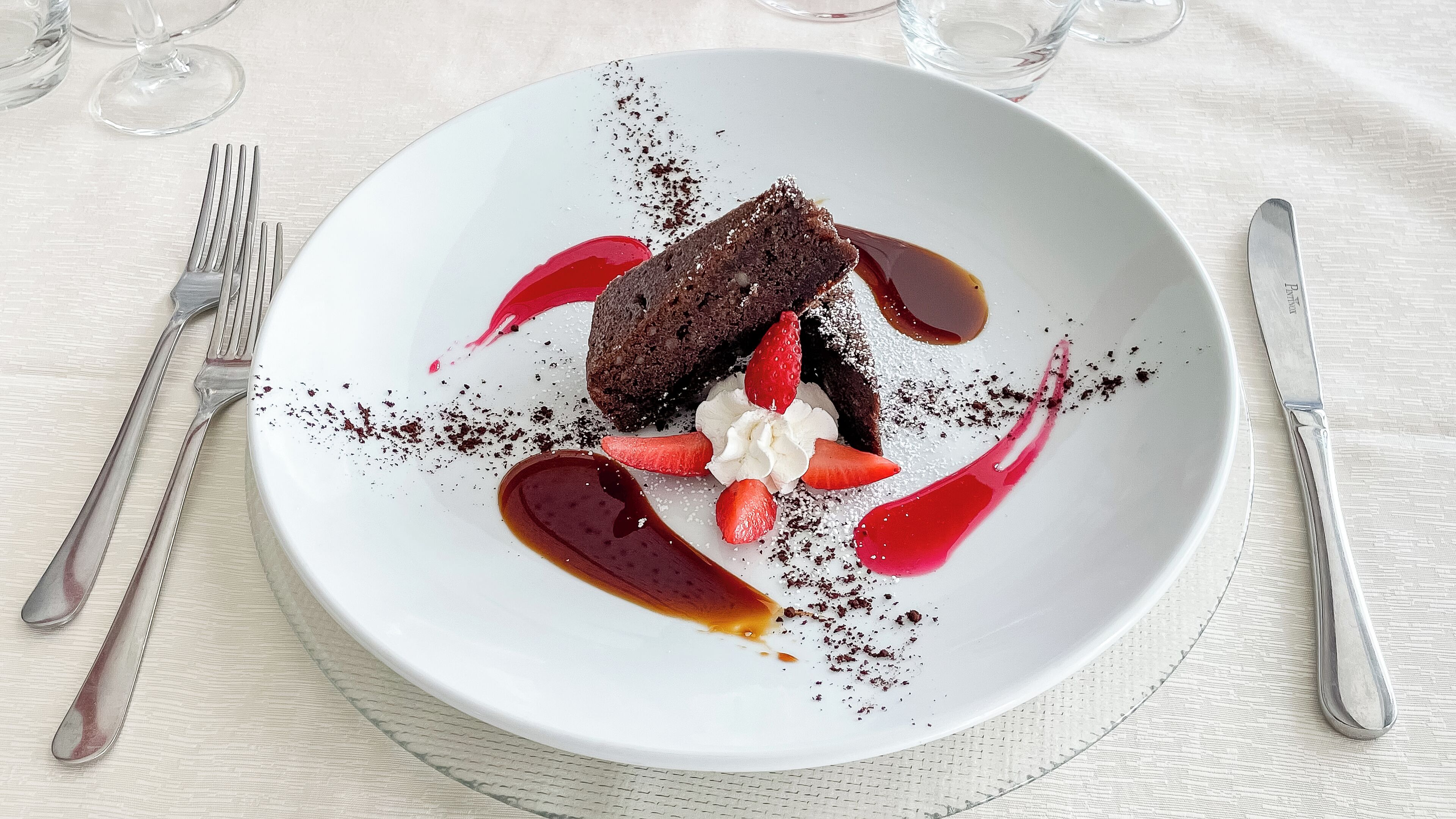 A dessert plate with a chocolate cake, strawberries, whipped cream, and sauce on a white plate.