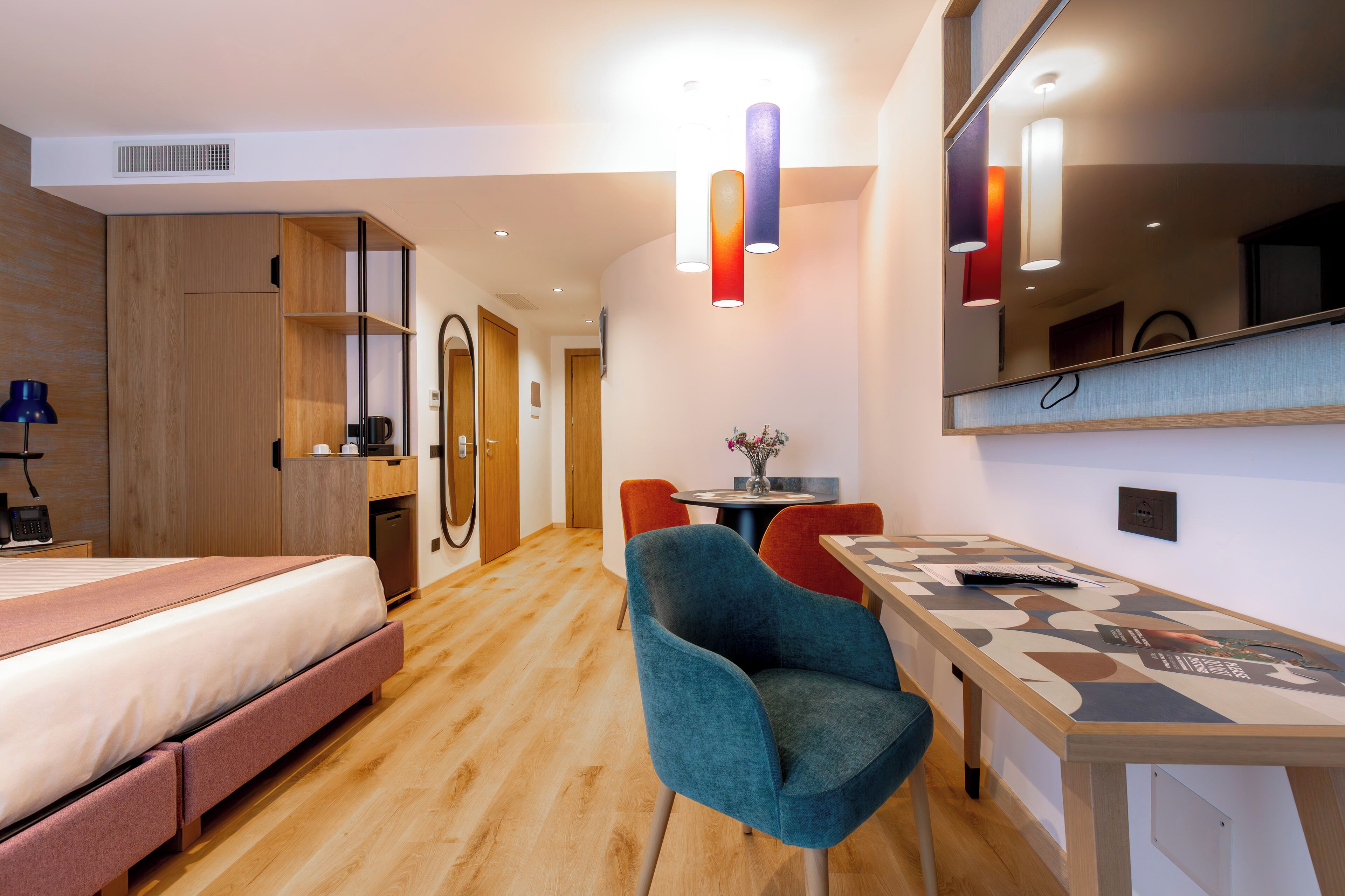 Una habitación de hotel moderna con una cama, un escritorio, una silla, una mesita y un espejo.
