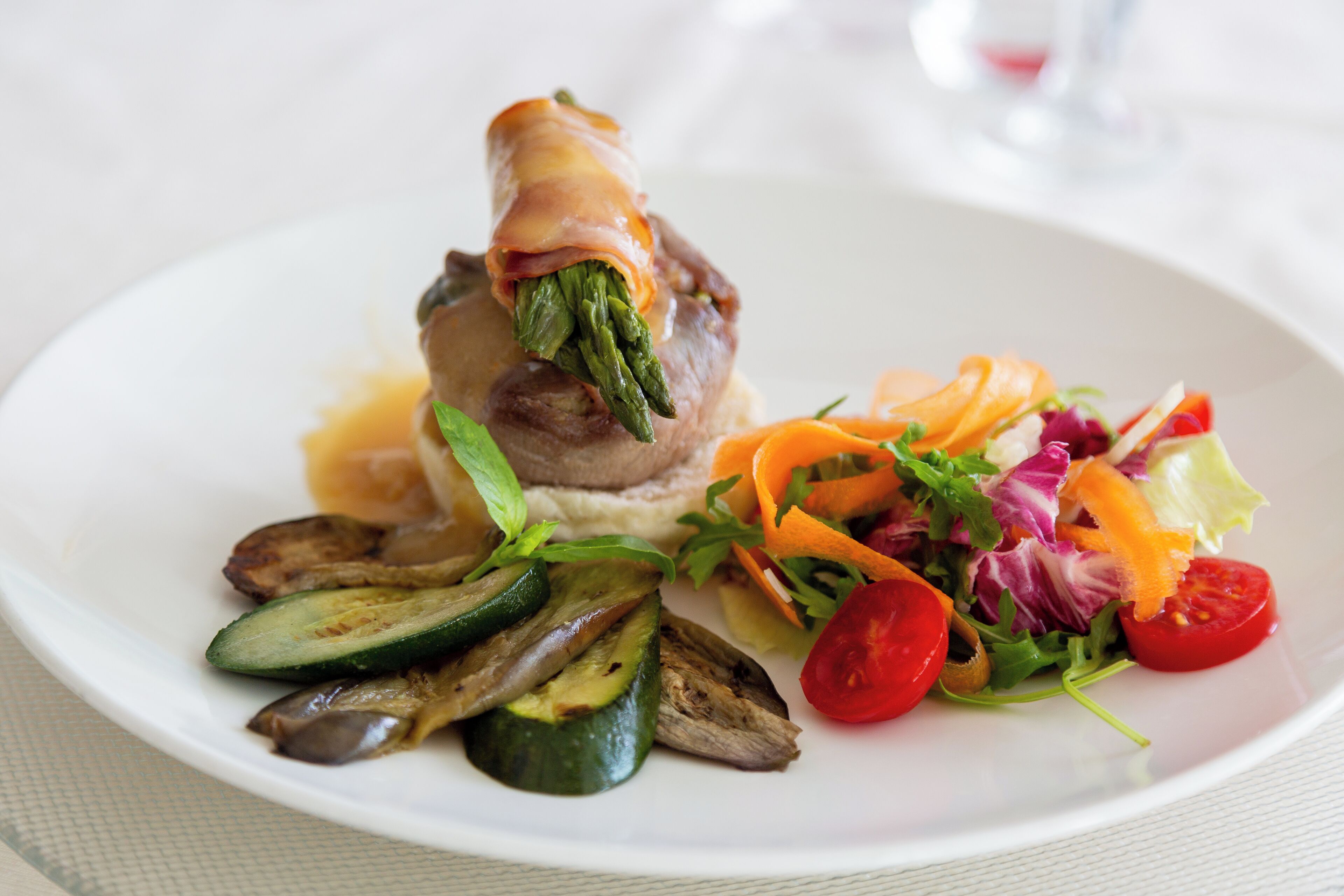 Ein Teller mit einem Fleischröllchen, Gemüse und Salat.