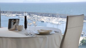 A table set for two with a view of the sea and a bridge.