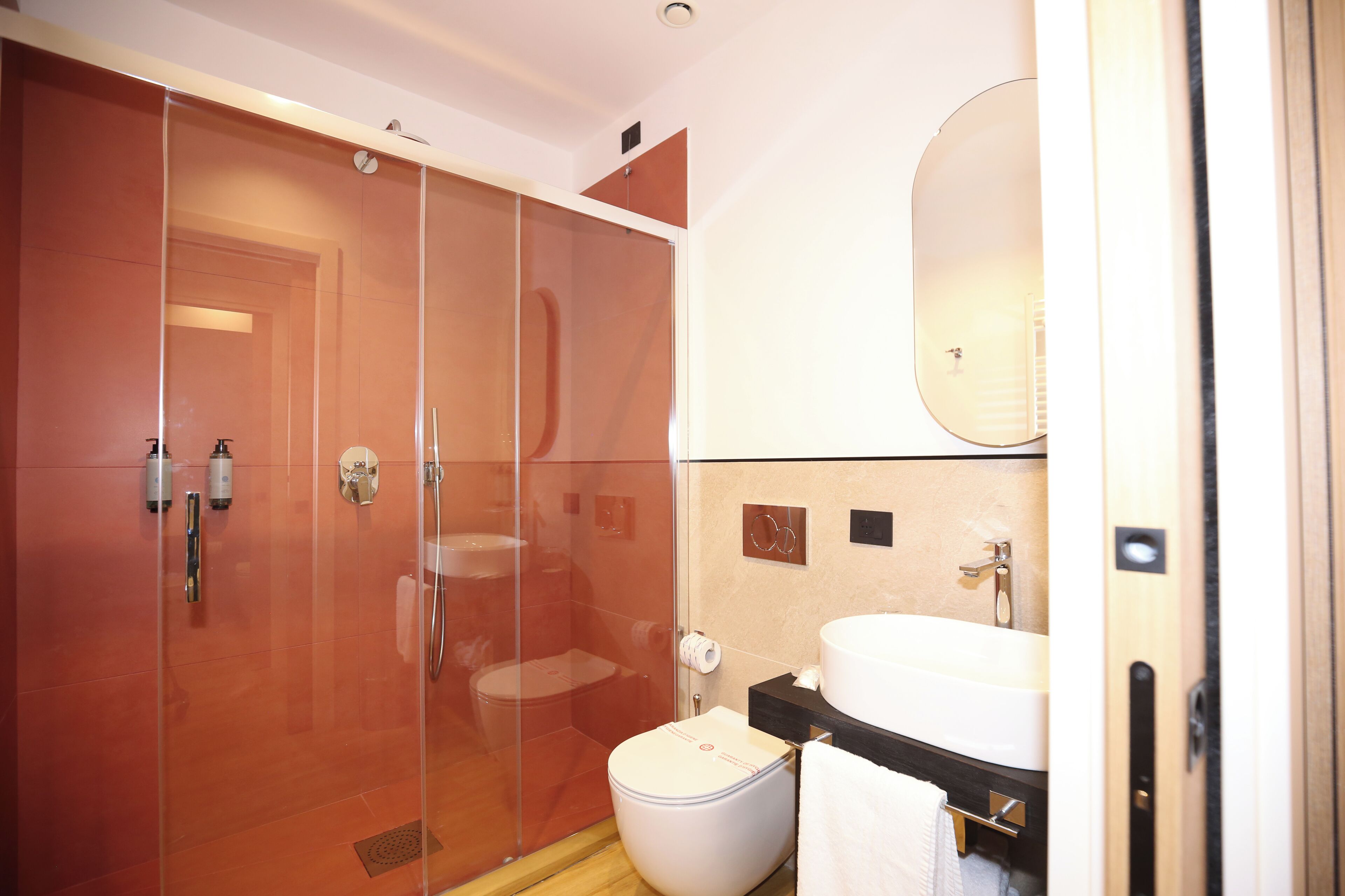 Une salle de bain moderne avec une douche à parois de verre, des toilettes blanches et un lavabo surmonté d’un miroir.