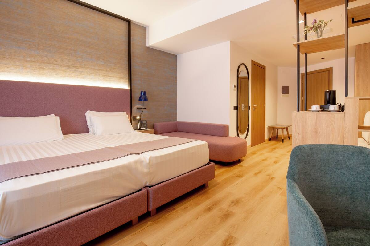 Una habitación de hotel moderna con una cama grande, una zona de estar, una mesita y un espejo.