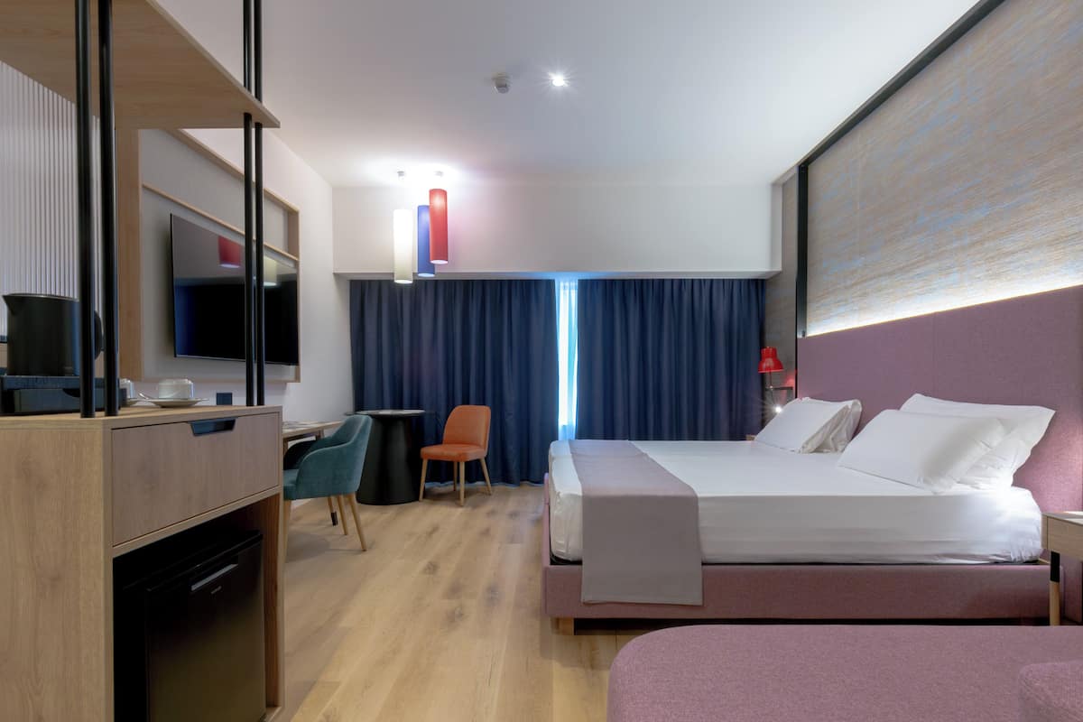 Habitación de hotel con cama, escritorio, silla, televisor y vistas al exterior.