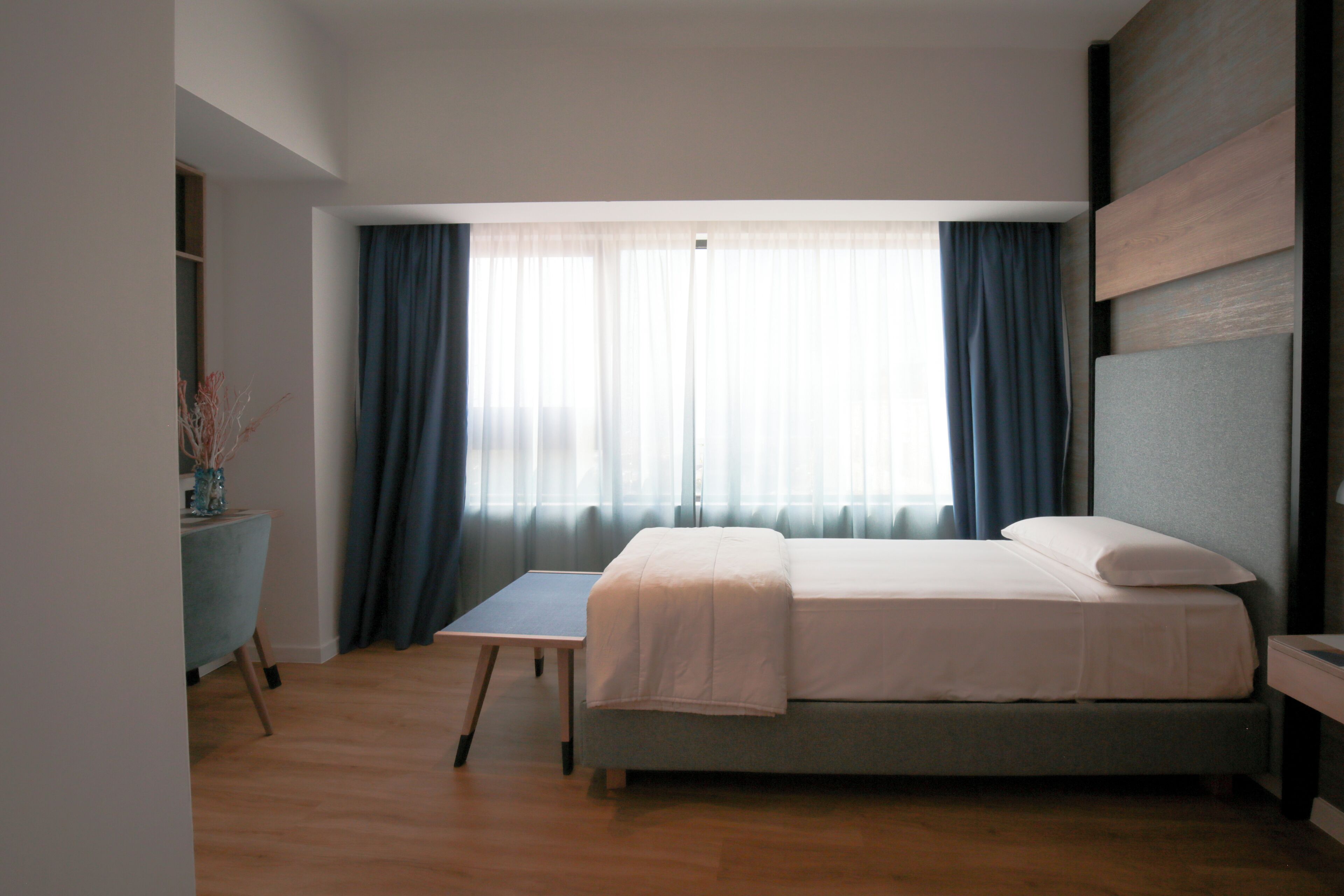 A bedroom with a bed, a desk, and a window with curtains.