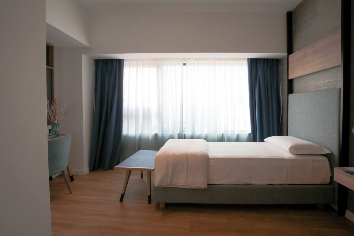 A bedroom with a bed, a desk, and a window with curtains.