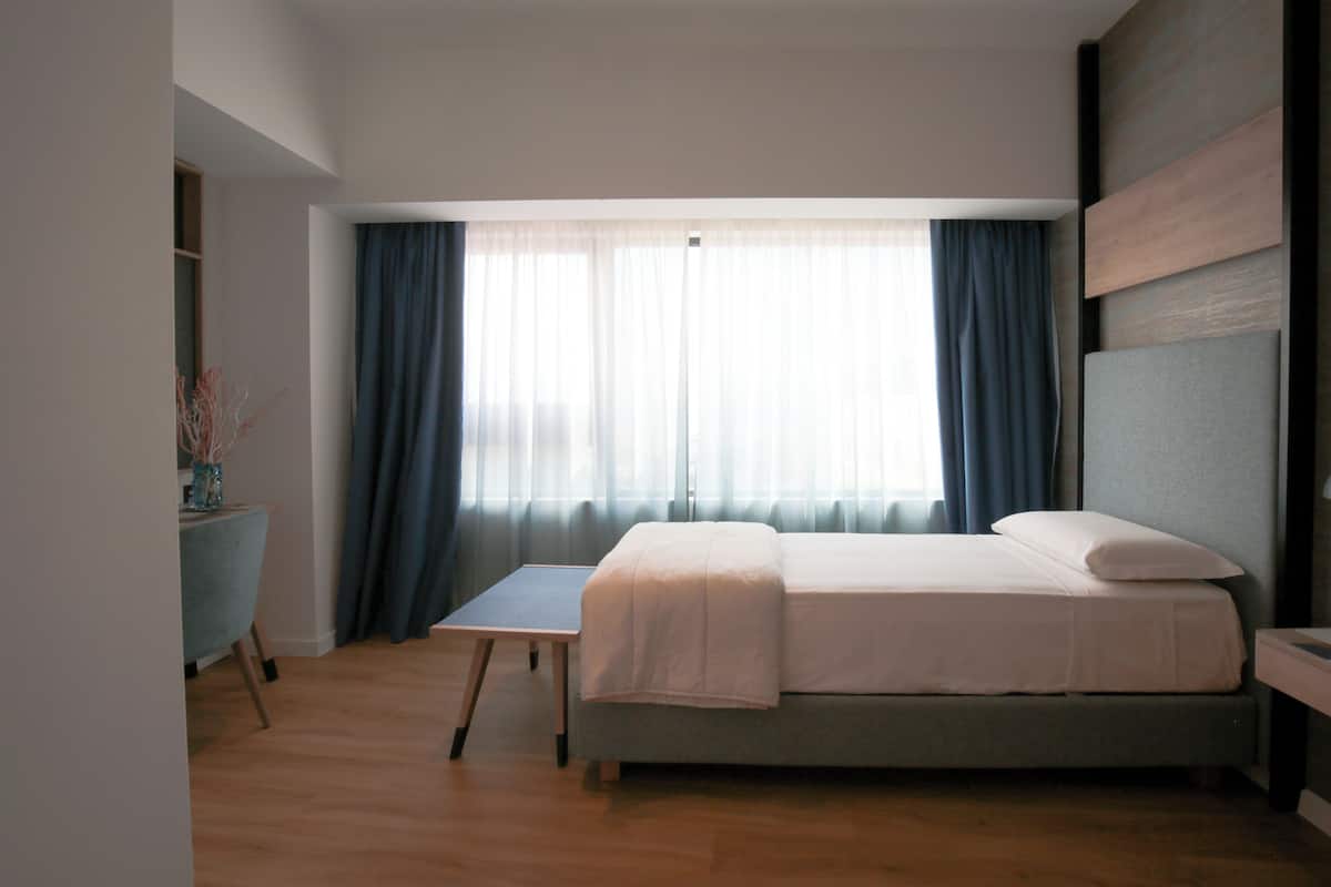 A bedroom with a bed, a desk, and a window with curtains.