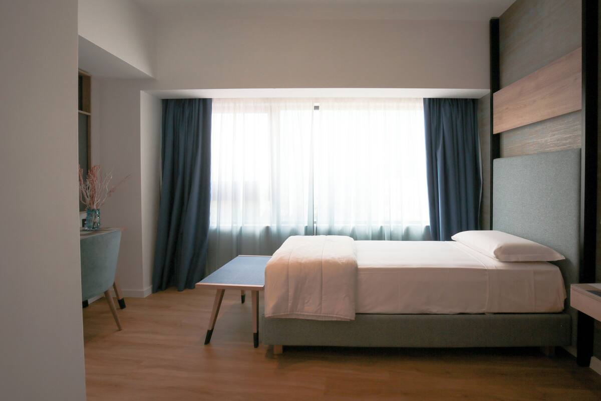 A modern bedroom with a bed, a desk, and a window with curtains.