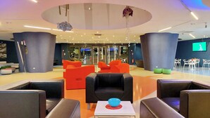 A modern lobby with black and orange seating, a central table with a blue bowl, and a large TV screen on the wall.