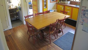 A dining area with a wooden table and red chairs, a kitchen with yellow cabinets, and a window with potted plants. - Tofino Trek Inn (Tofino)