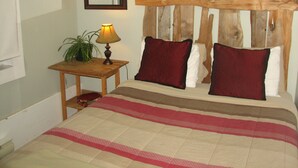 A bedroom with a wooden headboard, a bedside table with a lamp, and a bed with a striped bedspread. - Tofino Trek Inn (Tofino)