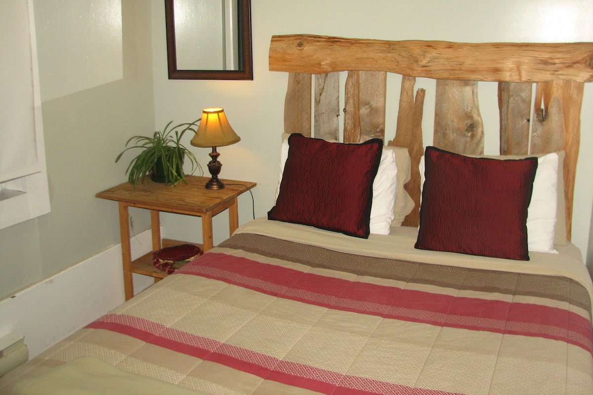 Un dormitorio con cabecera de madera, una mesita de noche con lámpara y una cama con colcha a rayas.