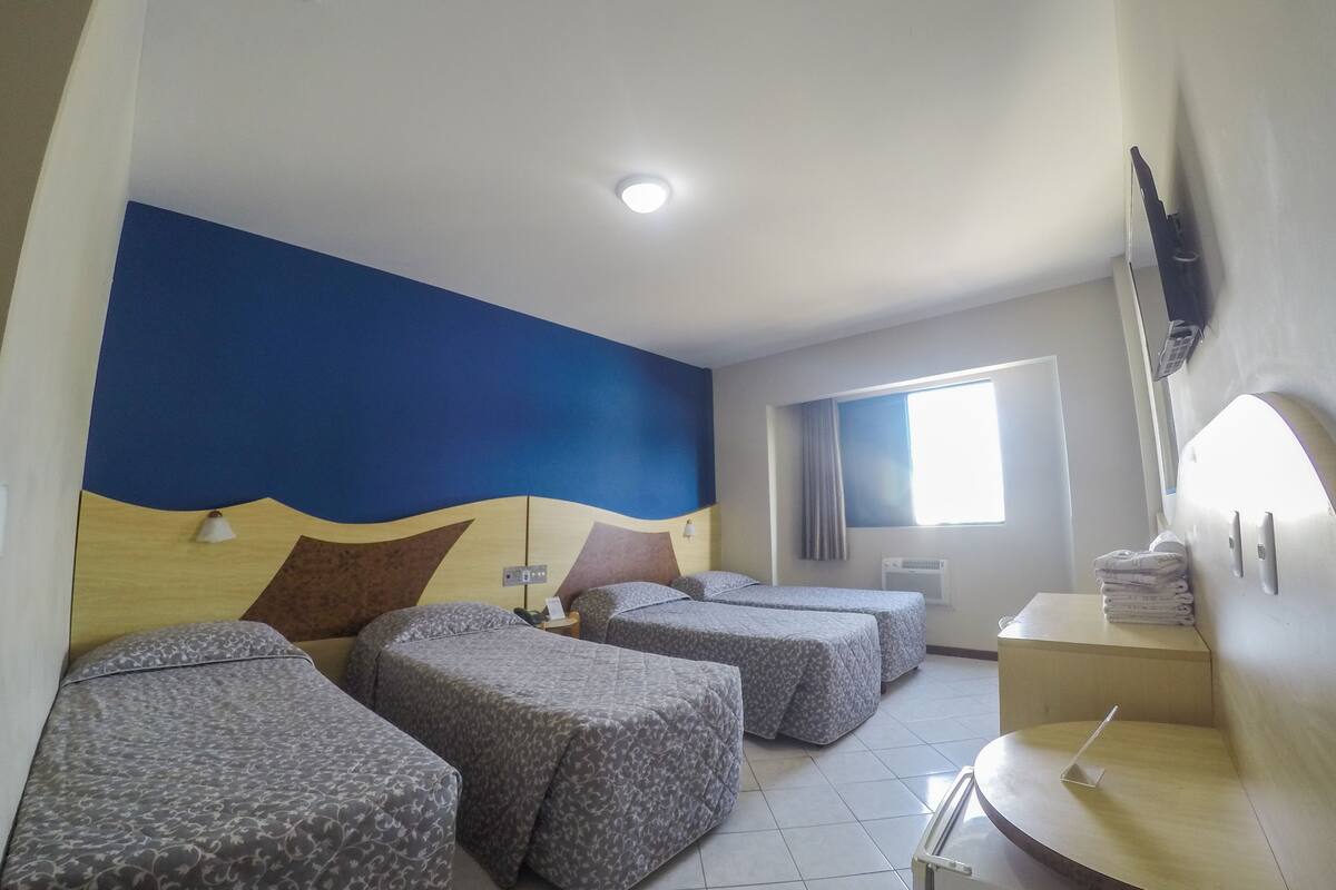 Een hotelkamer met twee eenpersoonsbedden, een klein bureau, een aan de muur bevestigde televisie en een raam met gordijnen.