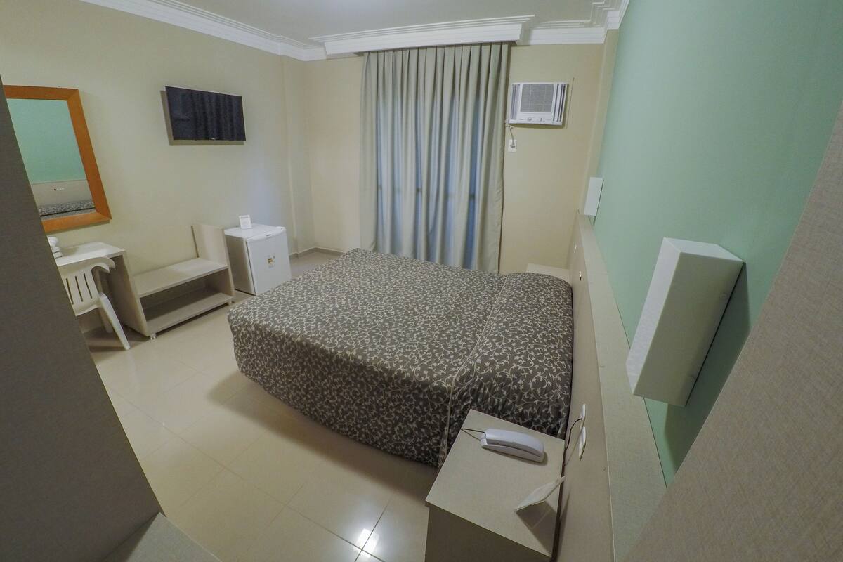 Hotelkamer met een bed, bureau, stoel, televisie en airconditioning.