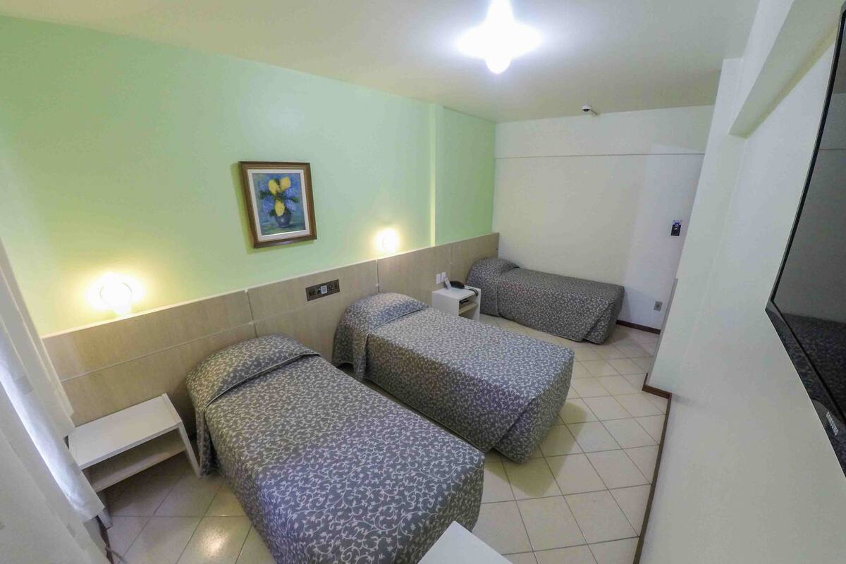 Hotelkamer met twee eenpersoonsbedden, een klein nachtkastje, een tv aan de muur en een stopcontact.