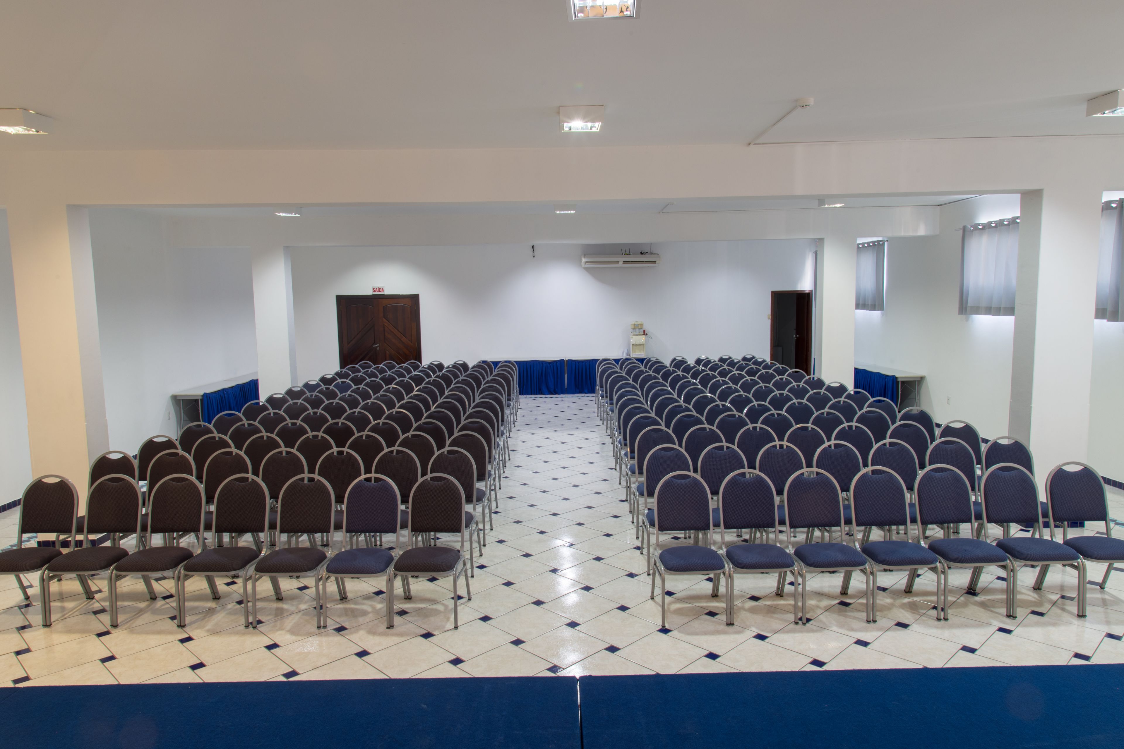 Une salle de conférence avec des rangées de chaises, une scène et un tapis bleu.