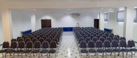 Une salle de conférence avec des rangées de chaises, une scène et un tapis bleu.
