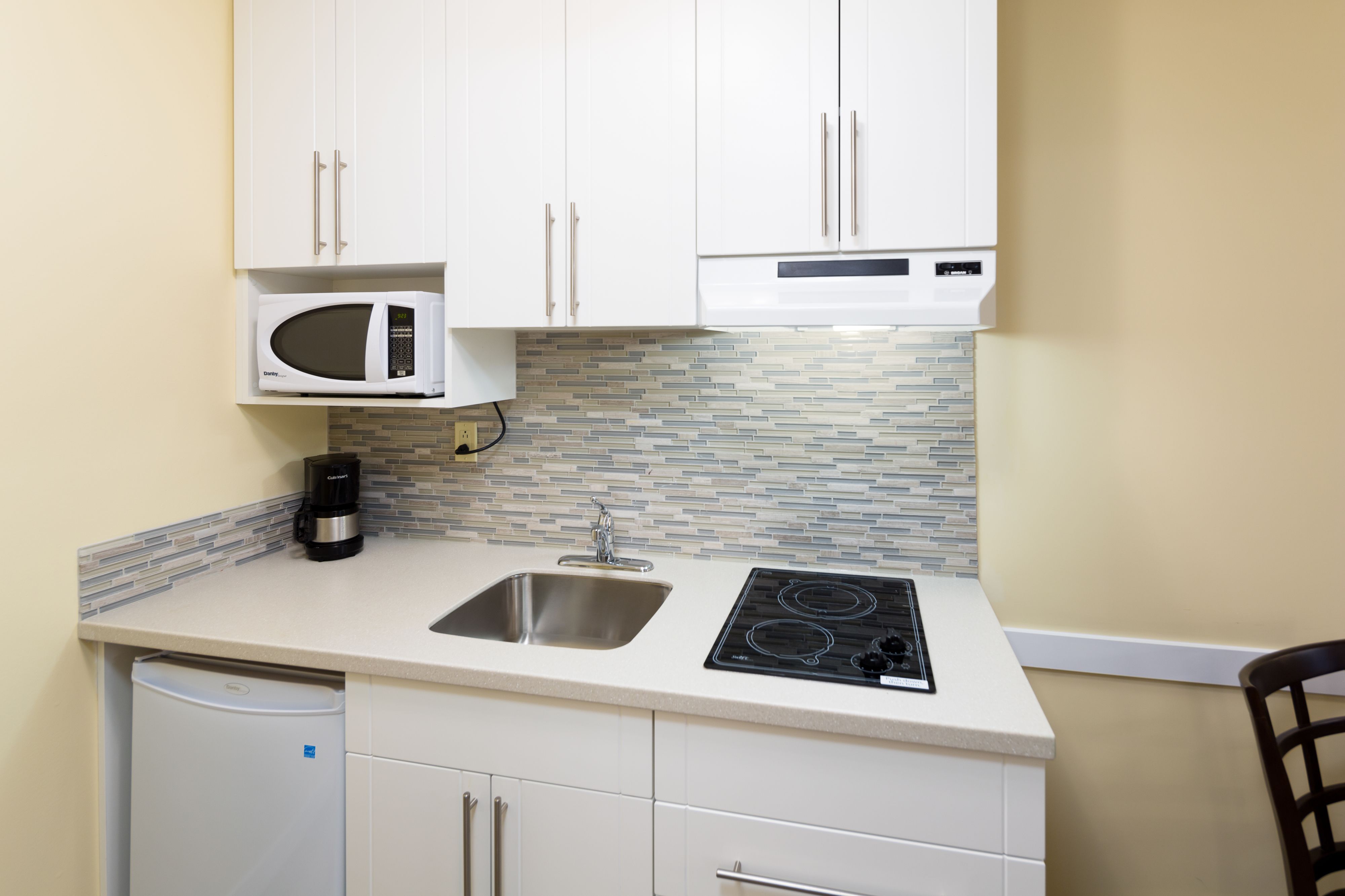 Una cocina compacta con armarios blancos, microondas integrado, cafetera, lavabo y estufa.