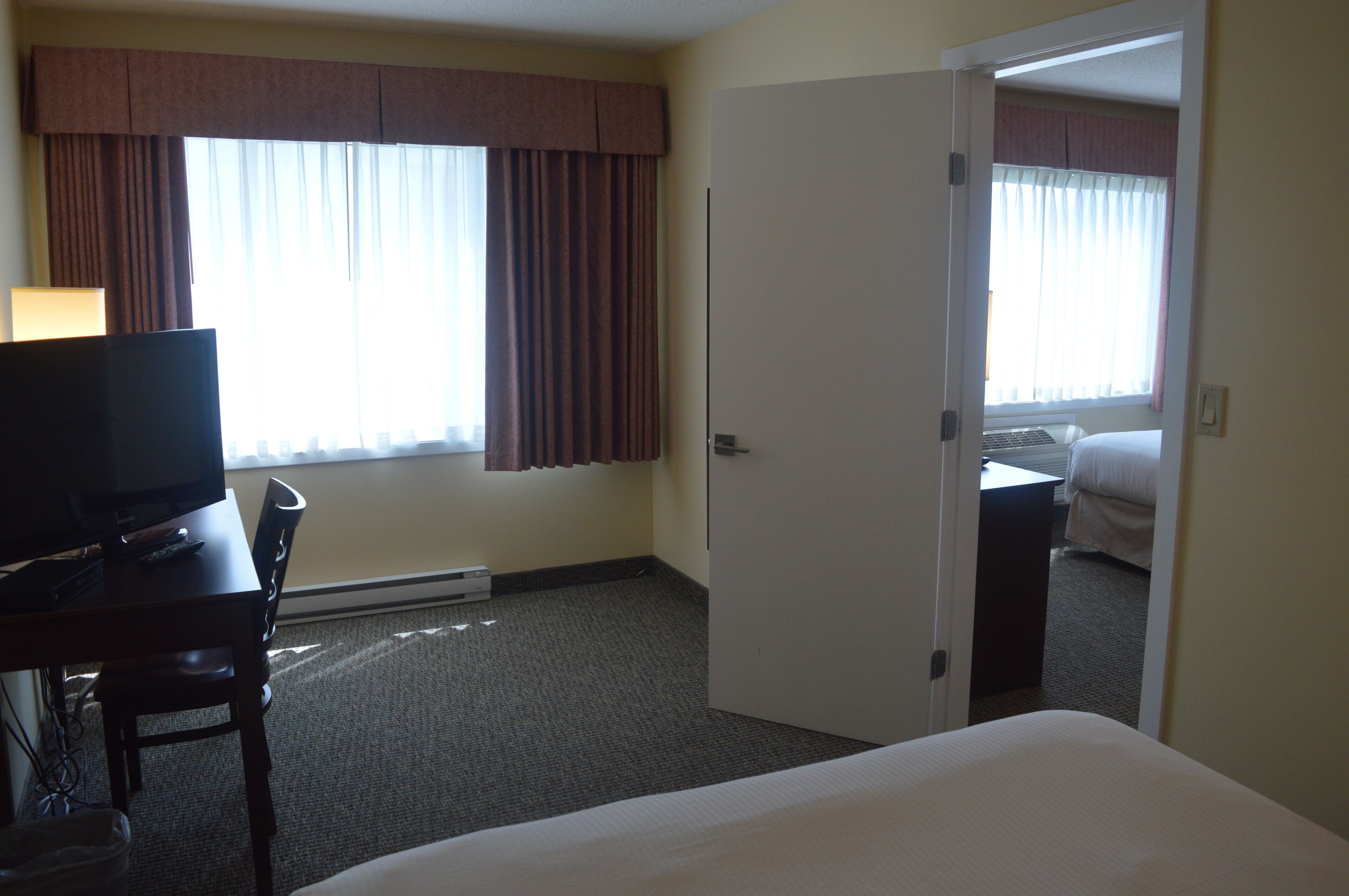 Una habitación de hotel con una cama, un escritorio con televisor y una ventana con cortinas.