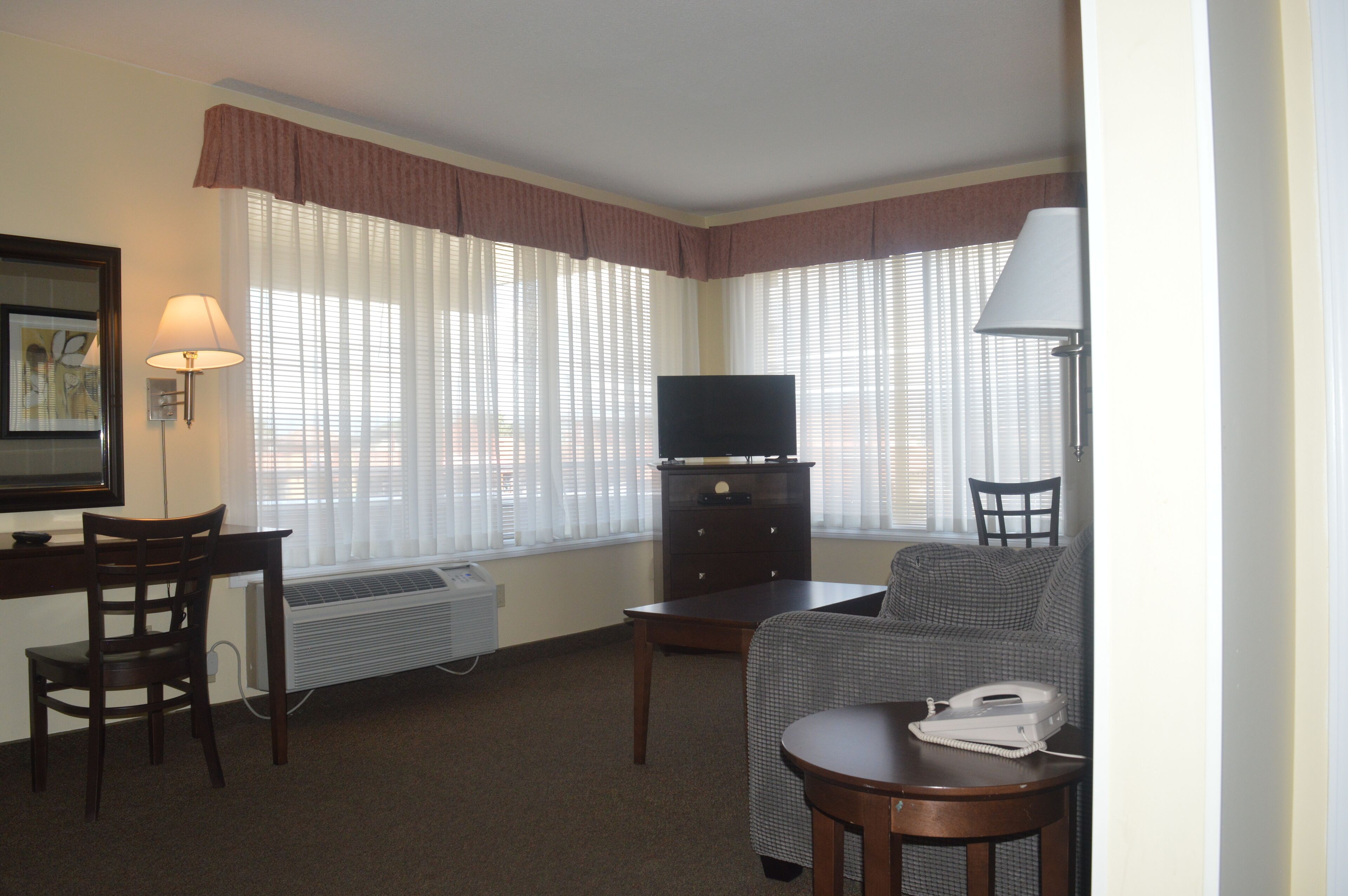 Ein Hotelzimmer mit Schreibtisch, Stuhl, Fernseher, Sofa und einem kleinen Tisch mit Telefon.