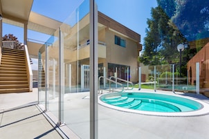 A modern building with a swimming pool, glass railings, and a wooden staircase.