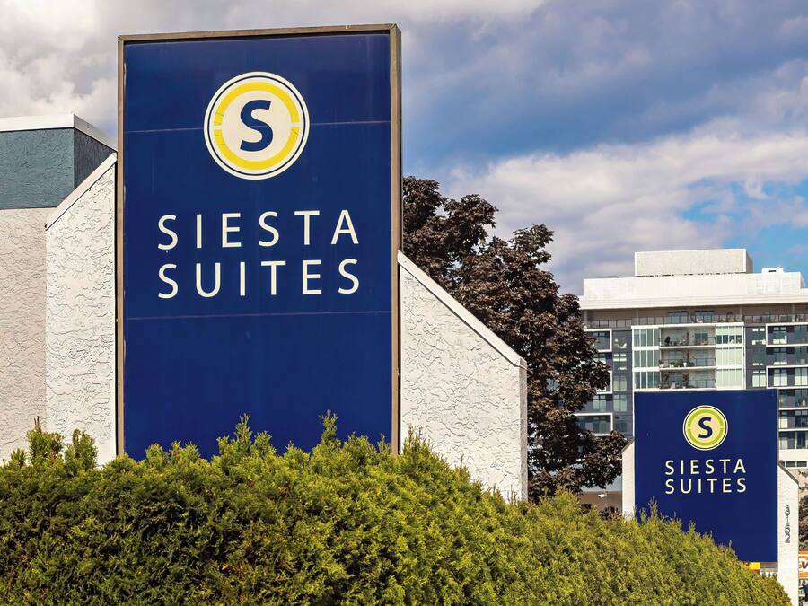 A large sign for Siesta Suites with a prominent logo, set against a backdrop of a building and trees.