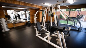 Une salle de sport équipée de divers appareils d’exercice, dotée d’un mur miroir et offrant une vue sur un jardin.