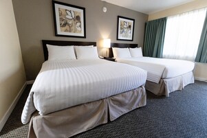 A hotel room with two beds, a nightstand with a lamp, and artwork on the walls.