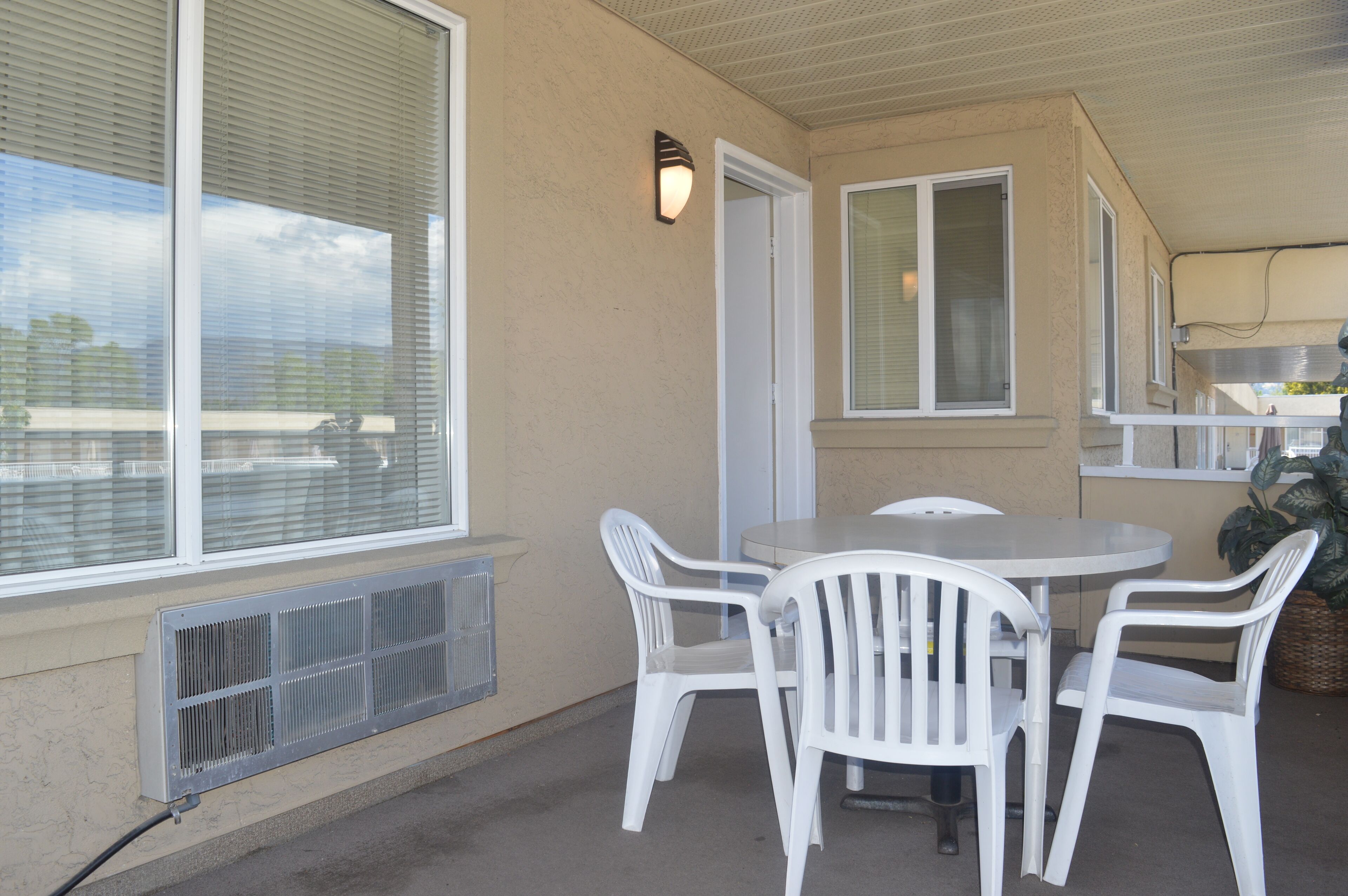 A covered patio with a round table and four white chairs, a vent, and a wall-mounted light fixture.
