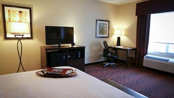 Habitación de hotel con cama, escritorio con computadora, televisor, lámpara de escritorio y aire acondicionado.