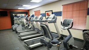 A row of stationary bikes in a gym with a tiled floor and a television mounted on the wall.