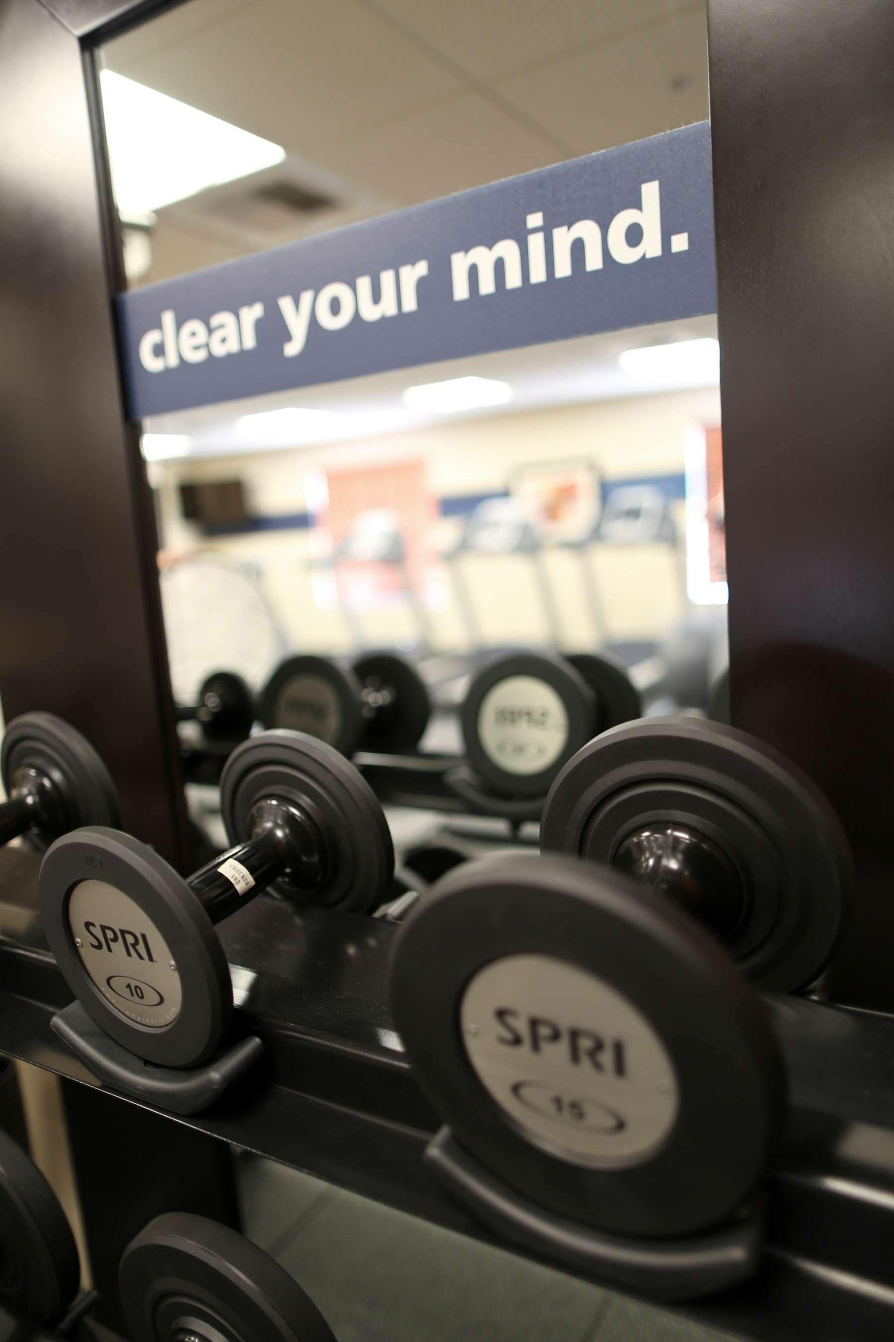 A weightlifting area with dumbbells labeled 'SPRI' and a sign that reads 'clear your mind.'