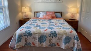 Ein Schlafzimmer mit einem Bett, zwei Nachttischen, einer Wanddekoration und einem Fenster mit Jalousien.