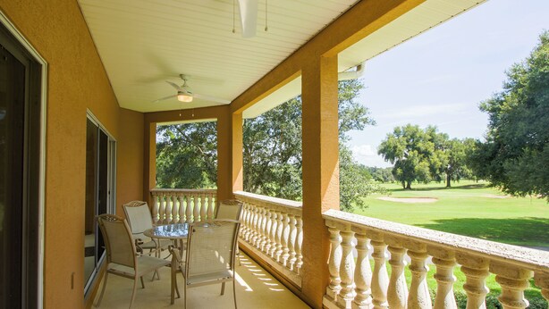 Ein überdachter Balkon mit Tisch und Stühlen, mit Blick auf einen Golfplatz.