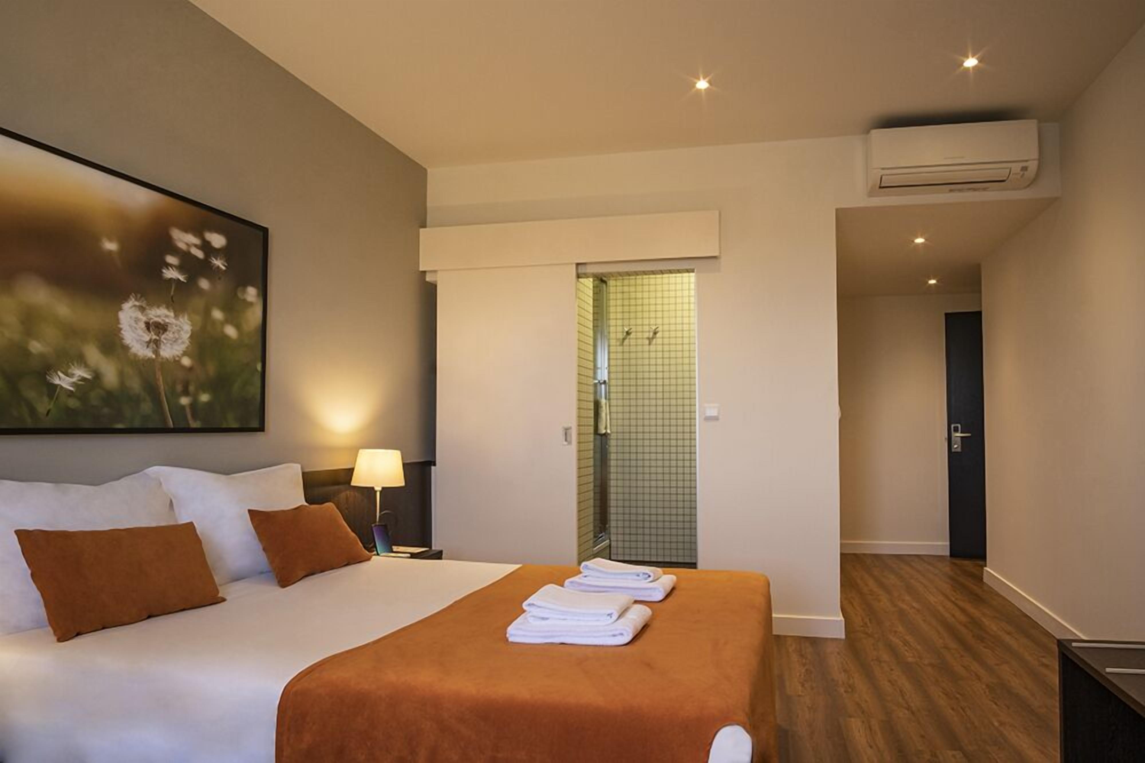 A hotel room with a bed, a nightstand, a lamp, a shower area, and an air conditioning unit.