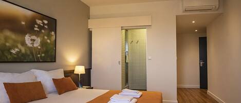A hotel room with a bed, a nightstand, a lamp, a shower area, and an air conditioning unit.