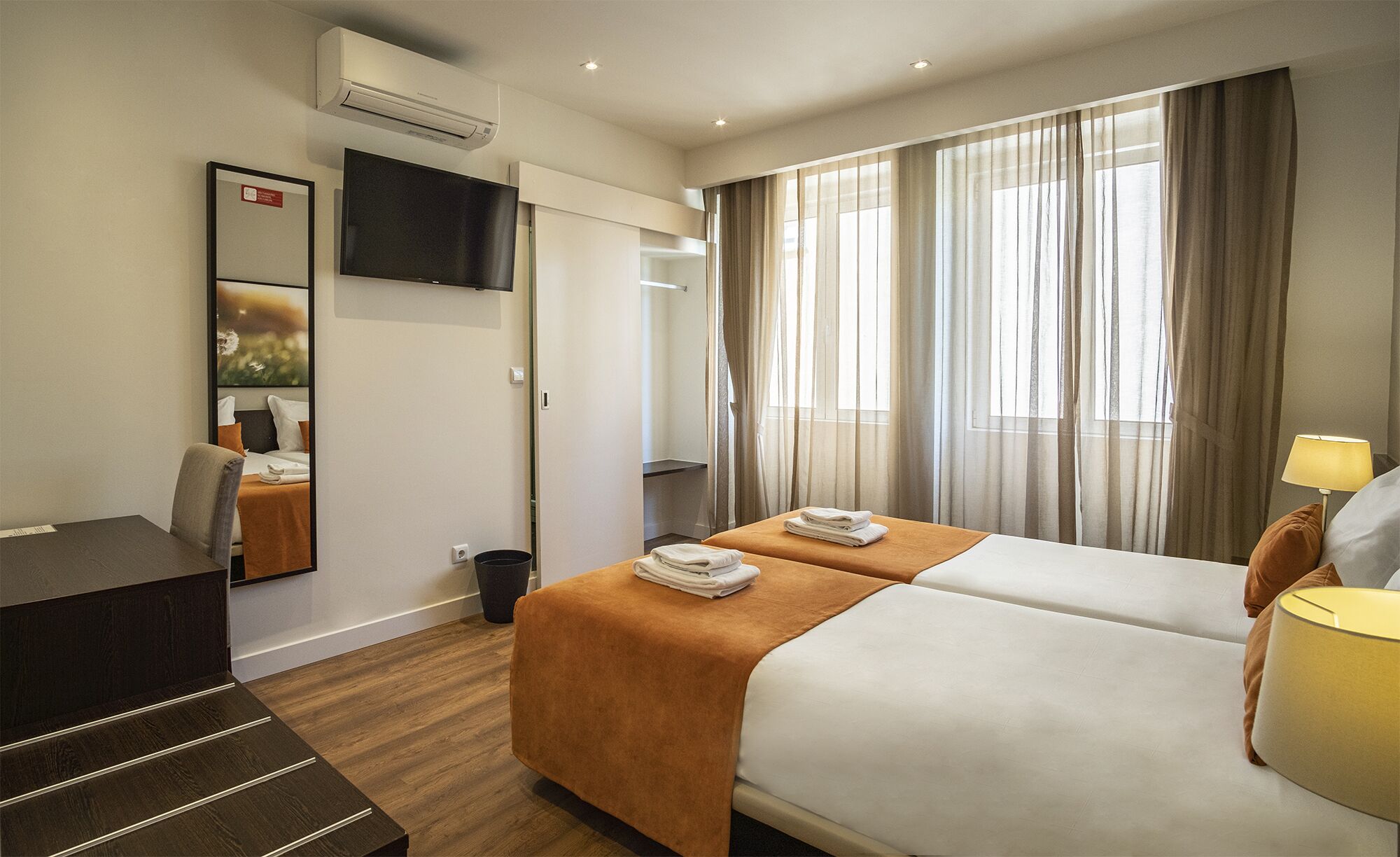 A hotel room with two beds, a desk, a TV, and a window with curtains.