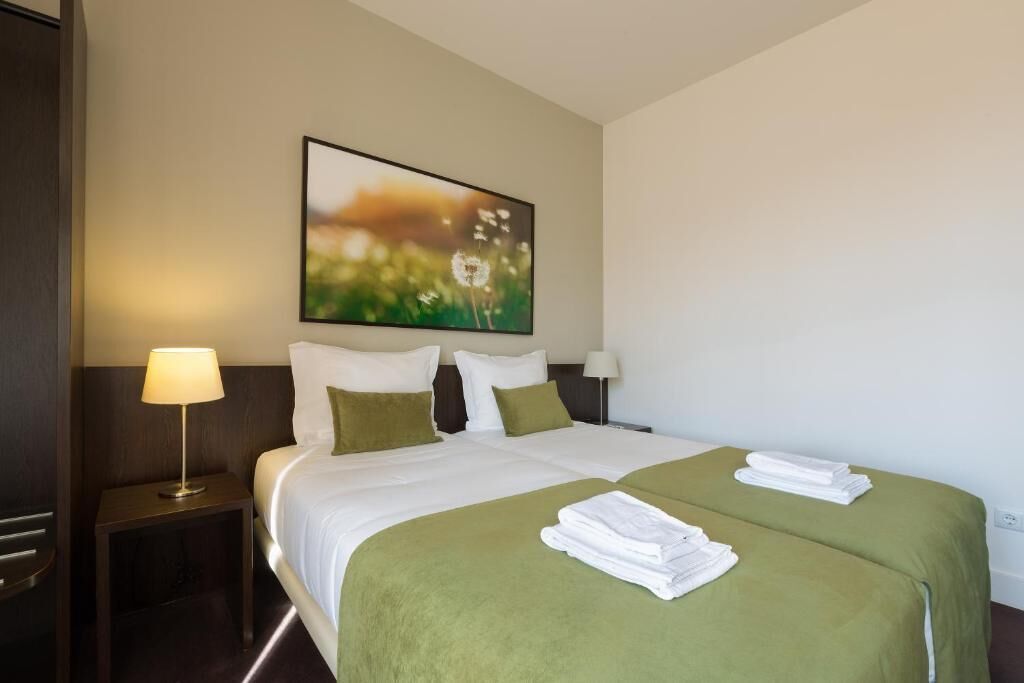 A hotel room with a large bed, two pillows, a nightstand with a lamp, and a painting on the wall.
