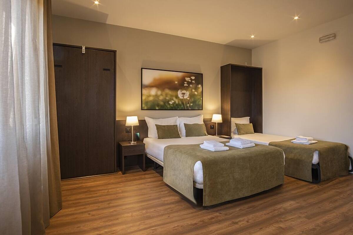 Habitación de hotel con dos camas, suelo de madera, un cuadro grande en la pared y un armario.
