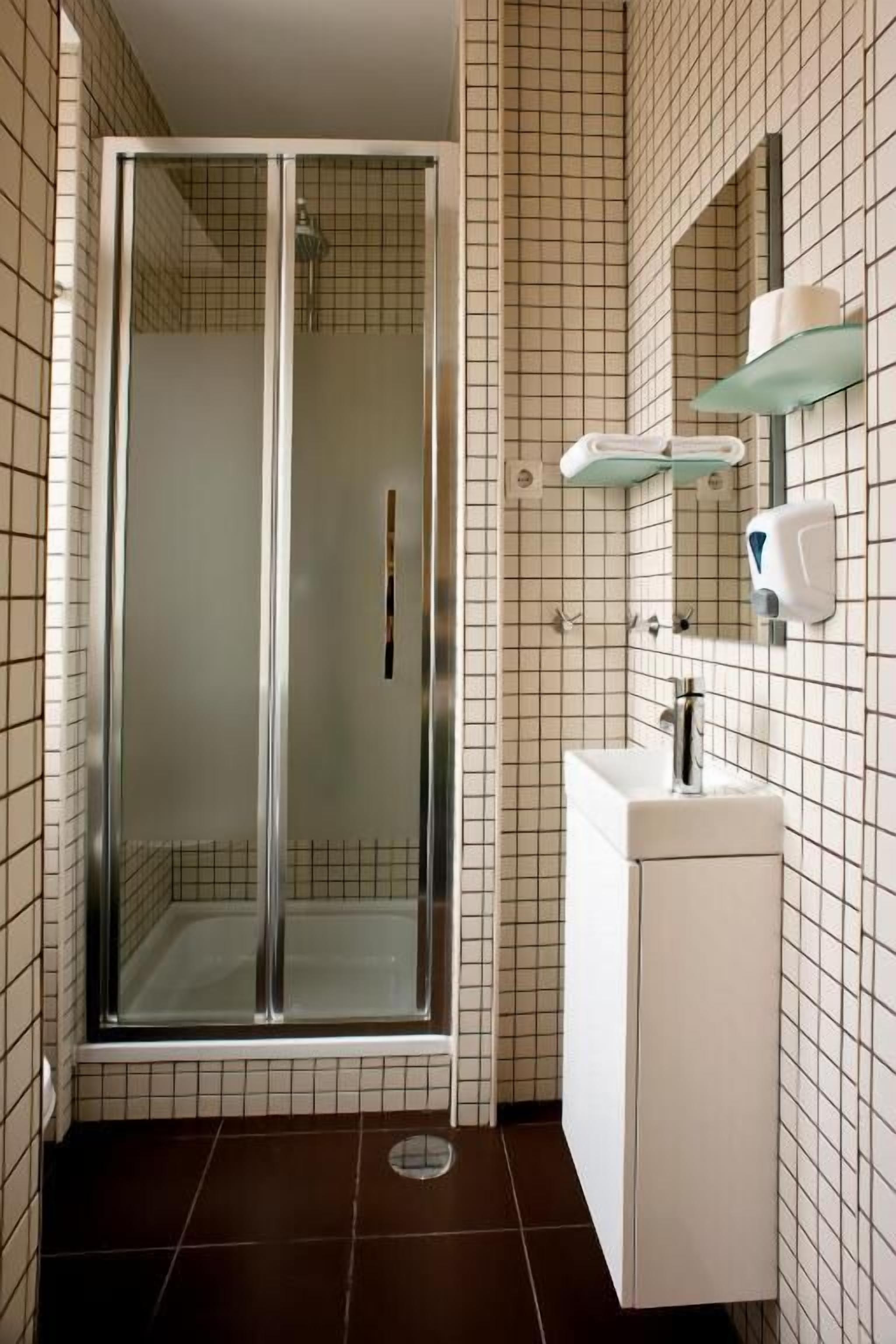 A bathroom with a glass-enclosed shower, a white sink with a mirror, and a soap dispenser on the wall.