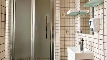 Une salle de bain avec une douche à parois de verre, un lavabo blanc avec un miroir et un distributeur de savon fixé au mur.