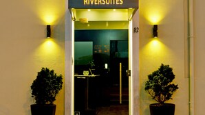 The entrance to Riversuites with a clear view of the interior through the glass doors, a black doormat, and two potted plants on either side. - Riversuites (Coimbra)