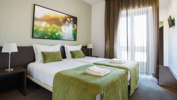Habitación de hotel con dos camas, un ventanal con cortinas, un cuadro en la pared y una mesita de noche con lámpara.