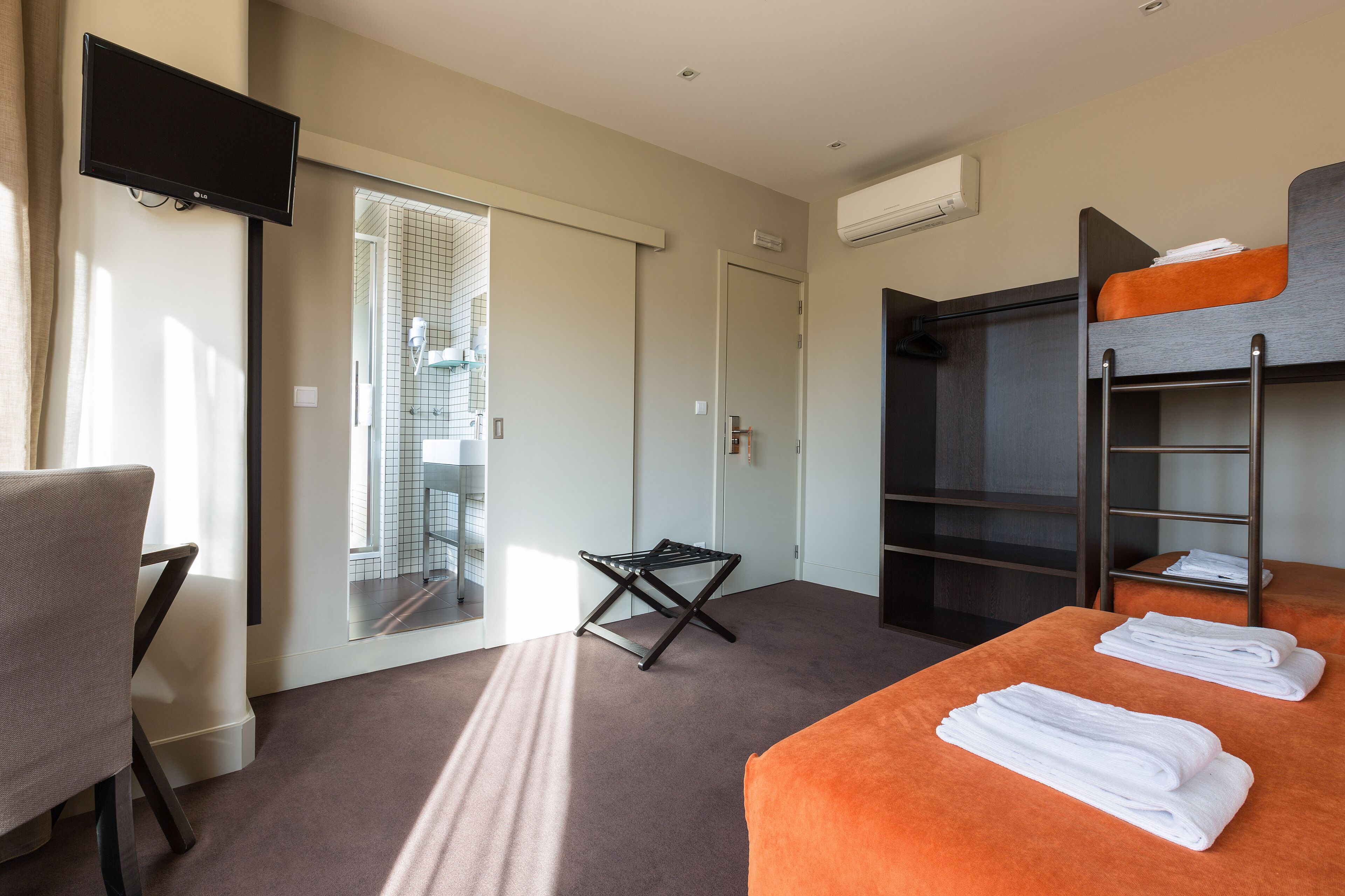 A hotel room with a bed, a chair, a TV, a wardrobe, and a balcony.