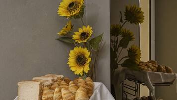 Un tavolo con pane e dolci, un vaso con girasoli e uno specchio che riflette la scena.