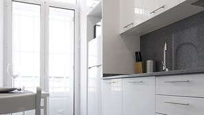 A modern kitchen with white cabinets, a granite countertop, and a dining area with a table and chairs. - Riversuites (Coimbra)