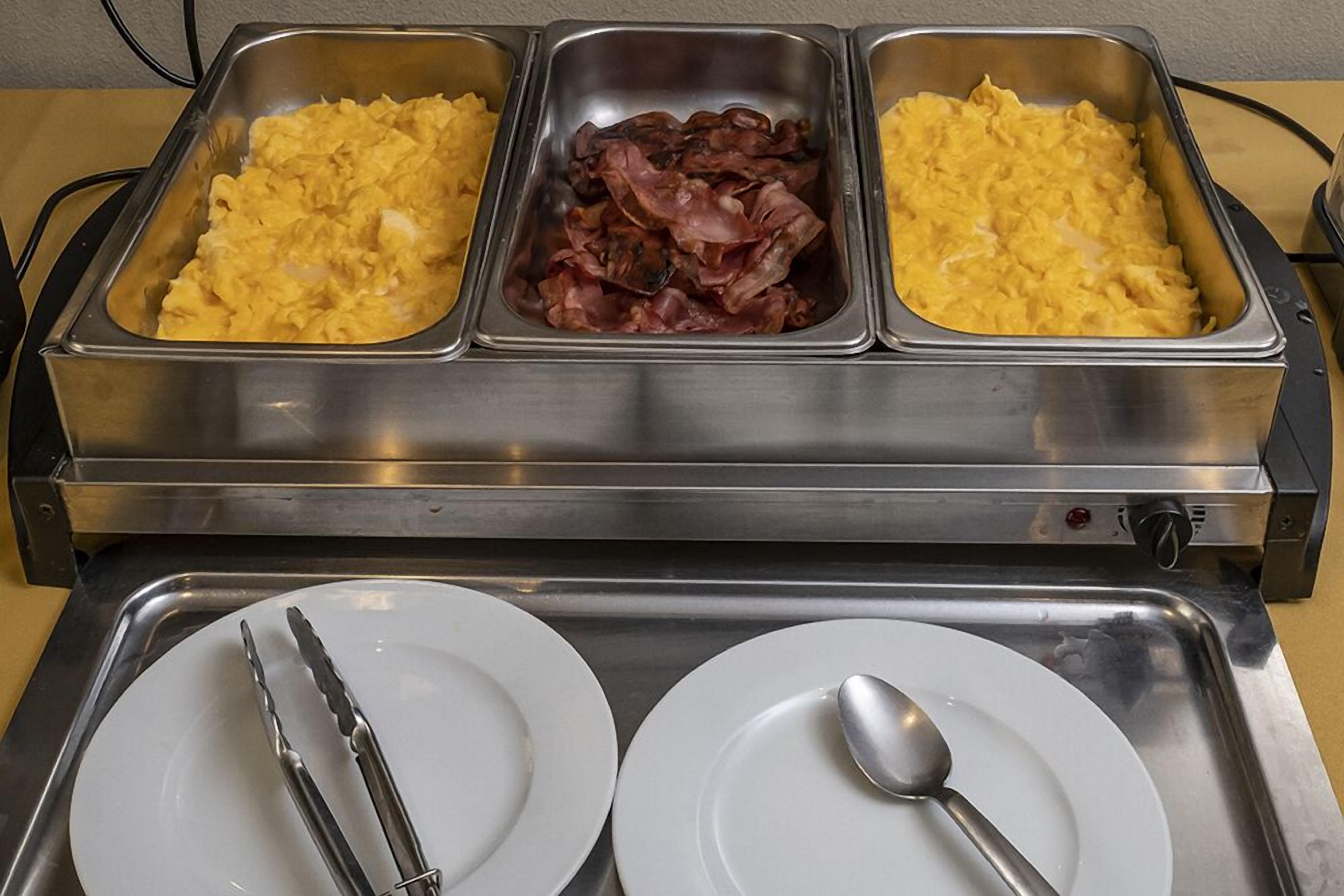 Un bufé con huevos revueltos, tocino y otro plato de huevos revueltos.