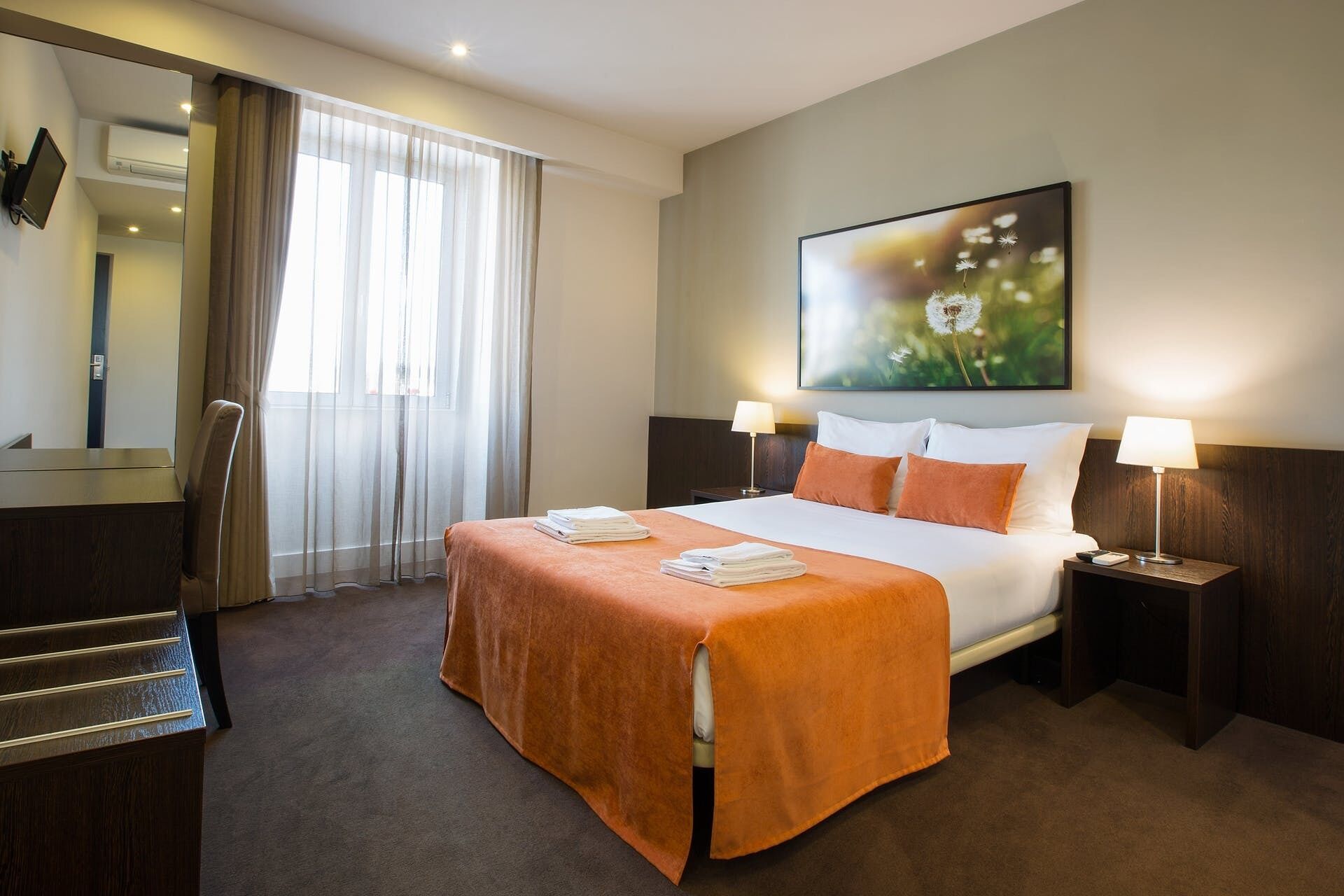 Habitación de hotel con cama, dos lámparas de noche, un cuadro en la pared, un escritorio y una silla.