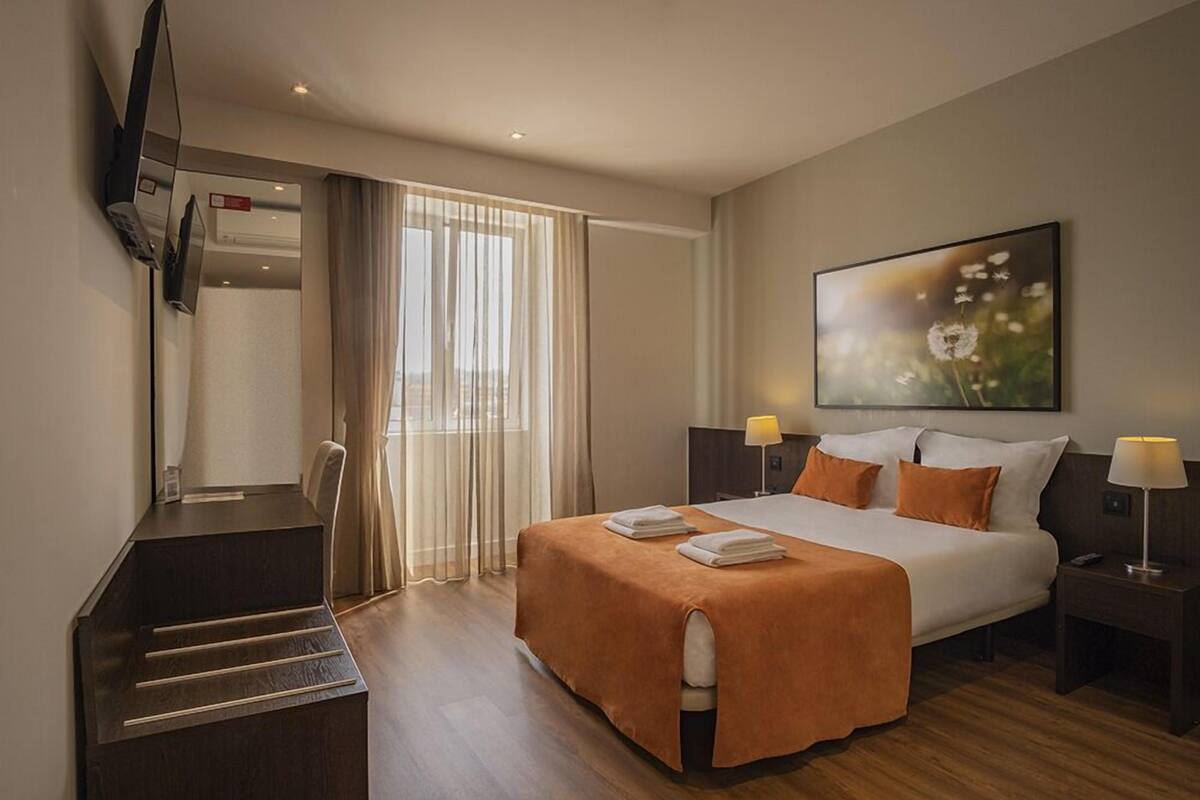 Una habitación de hotel con una cama, un escritorio, una silla, un televisor y un cuadro en la pared.