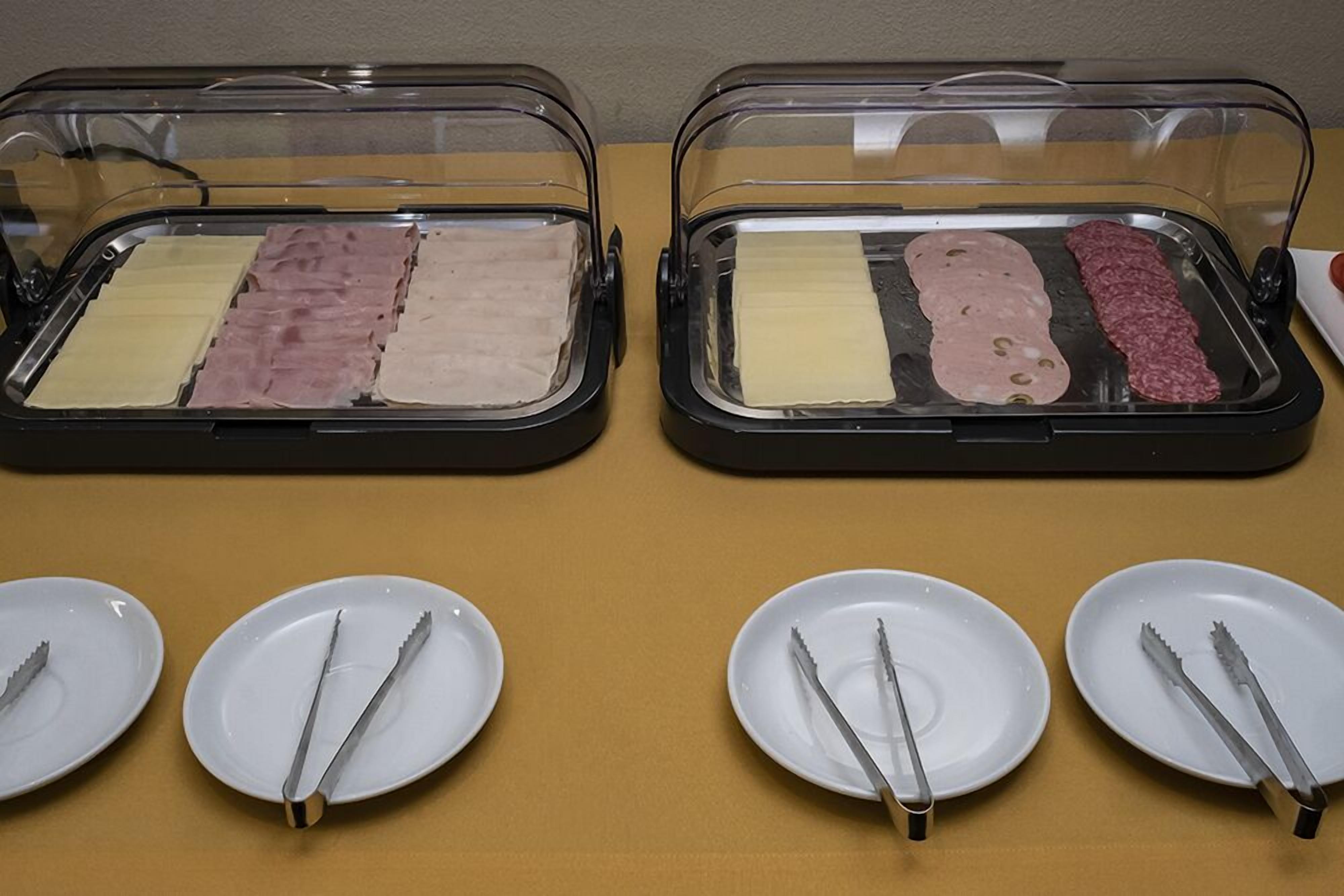 Dos vitrinas de vidrio con diversos tipos de carne y queso, acompañadas de platos blancos y cubiertos.